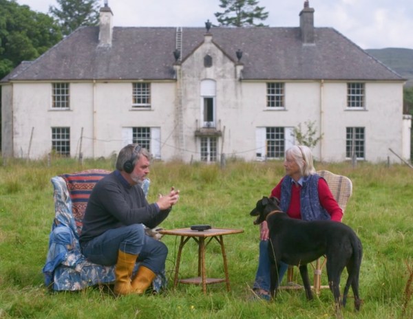 Alasdair and Andrena sit on chairs in a field infront of a large house.